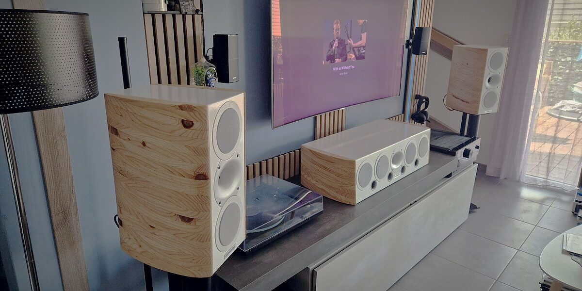 Enceinte centrale home cinéma Gautier Audio, façade blanche et joues en bois massif, posée sous un écran dans un salon